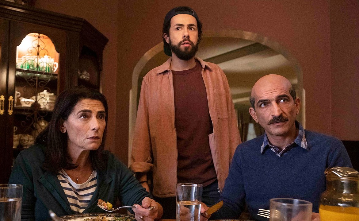 A still of three characters in a dining room staring off camera