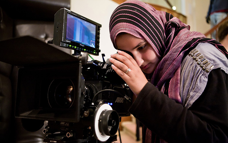 Lena Khan looking into viewfinder on set