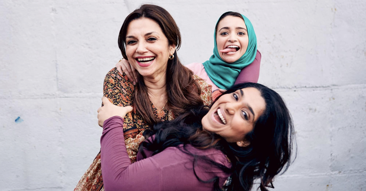 Three smiling woman embracing, one is wearing a hijab