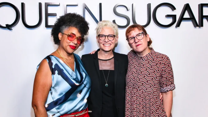Three women pose in front of a Queen Sugar sign