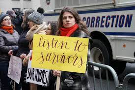 Woman holding a sign that reads 'listen to survivors'