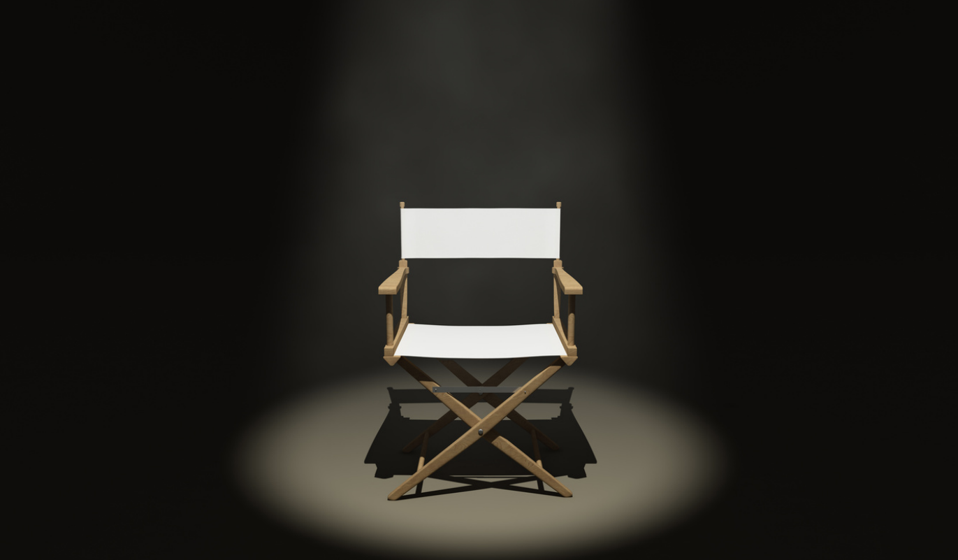 A white cloth director's chair spotlit against a black background.